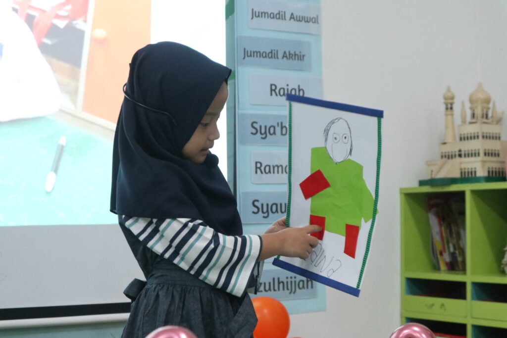 Seorang murid perempuan TK Islam Al Azhar 12 Cikarang sedang mempresentasikan karya seni kolasenya di depan kelas.