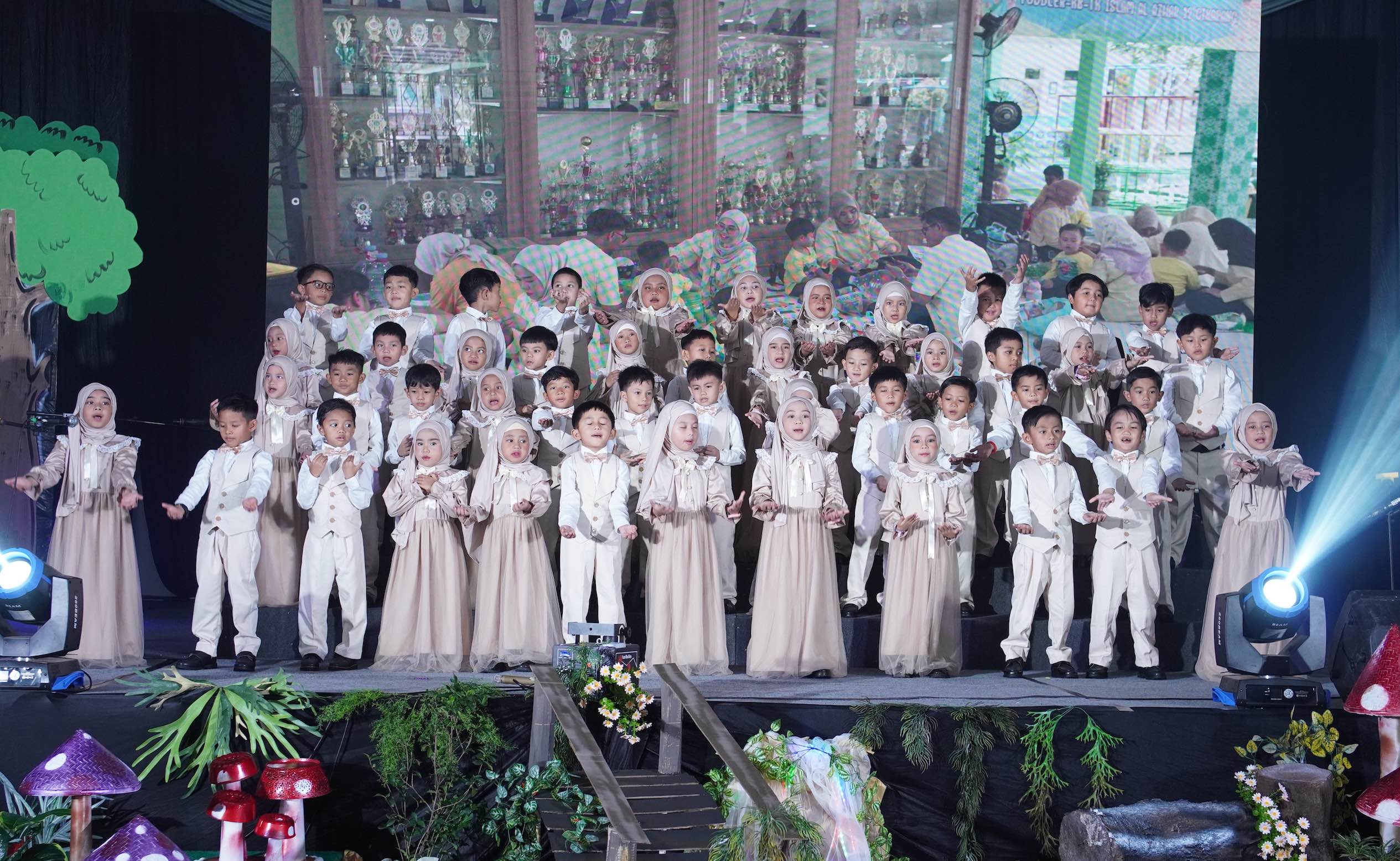 Murid-murid berbusana krem berbaris rapi di atas panggung menyanyikan lagu perpisahan dengan gestur tangan terbuka.