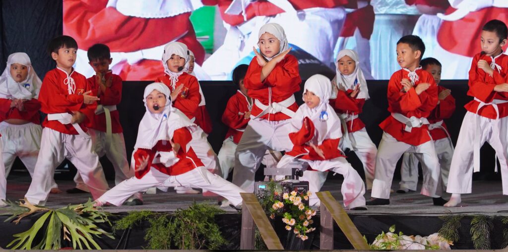 Murid-murid berseragam merah putih memperagakan jurus seni bela diri Tapak Suci di atas panggung.