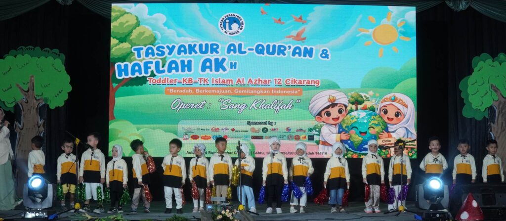 Murid-murid TK berbaris di panggung memegang pom-pom di depan layar latar bertuliskan Tasyakur Al-Qur'an.