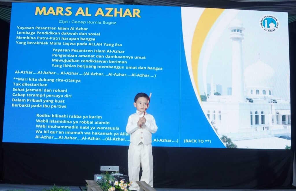 Seorang murid laki-laki menyanyikan Mars Al Azhar di atas panggung dengan latar layar lirik lagu.
