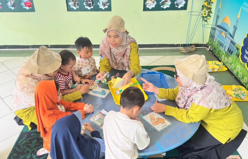 Guru membimbing murid dalam kegiatan belajar kelompok di dalam kelas yang nyaman.