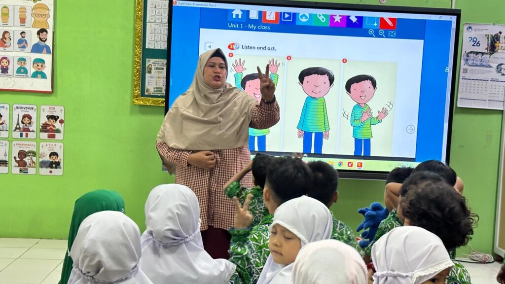 Guru memberikan contoh gerakan untuk membantu murid memahami kosakata dan instruksi bahasa Inggris.